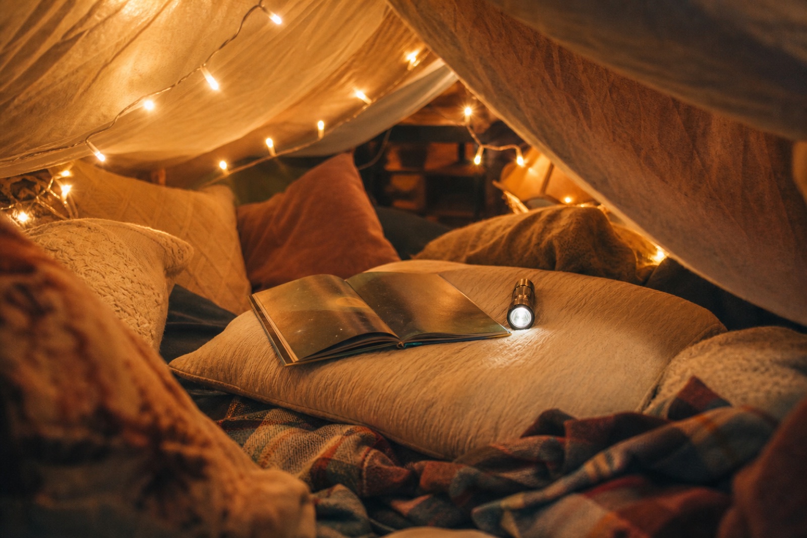 A blanket fort glowing with string lights and an open storybook